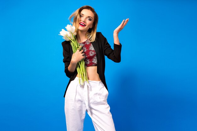 Retrato de jovem elegante com maquiagem brilhante e blazer escuro, segurando flores brancas