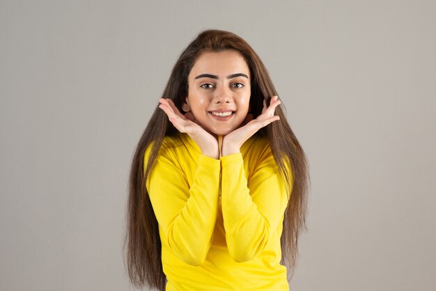 Retrato de jovem em amarelo top olhando e sorrindo na parede cinza.