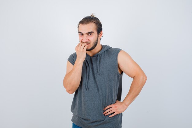 Retrato de jovem em forma de homem roendo unhas com capuz sem mangas e parecendo estressado na frente