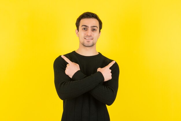 Retrato de jovem em moletom preto em pé e posando para a câmera na parede amarela