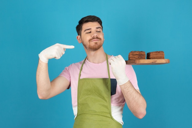 Retrato de jovem em um azul segurando fatias de bolo e apontando o dedo para ele.