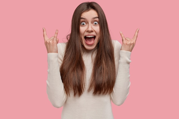 Retrato de jovem emotiva de cabelos escuros fazendo gestos de rock n roll, escuta heavy metal e exclama em voz alta