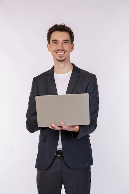 Retrato de jovem empresário sorridente e bonito segurando laptop nas mãos digitando e navegando em páginas da web isoladas em fundo branco