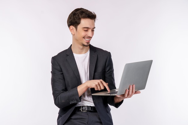 Retrato de jovem empresário sorridente e bonito segurando laptop nas mãos digitando e navegando em páginas da web isoladas em fundo branco