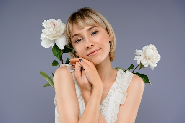 Retrato de jovem entre flores ao longo da parede cinza