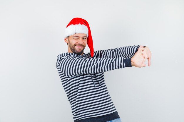 Retrato de jovem esticando as mãos para ter força e mobilidade com um capuz, chapéu de Papai Noel e parecendo relaxado