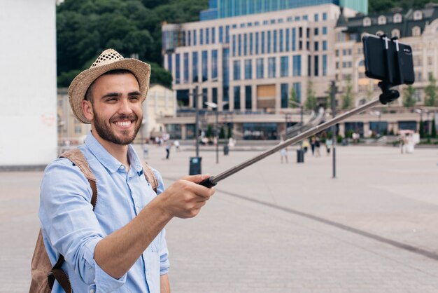 Retrato de jovem feliz carregando mochila tomando selfie com smartphone