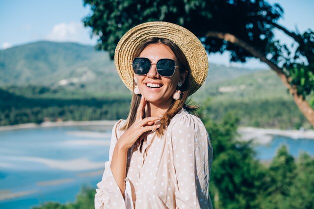 Retrato de jovem feliz com vestido de verão, óculos escuros e chapéu de palha