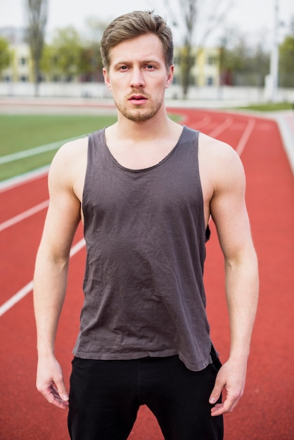 Retrato de jovem fitness em pé na pista de campo