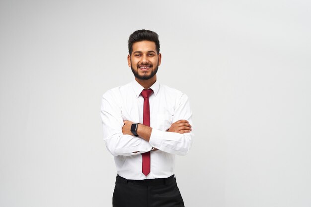 Retrato de jovem gerente indiano de t-shirt e gravata, braços cruzados e sorrindo na parede branca isolada