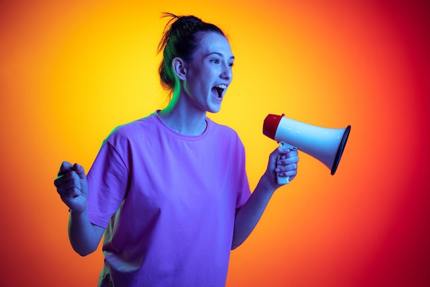 Retrato de jovem gritando no megafone posando isolado sobre fundo amarelo vermelho gradiente em neon