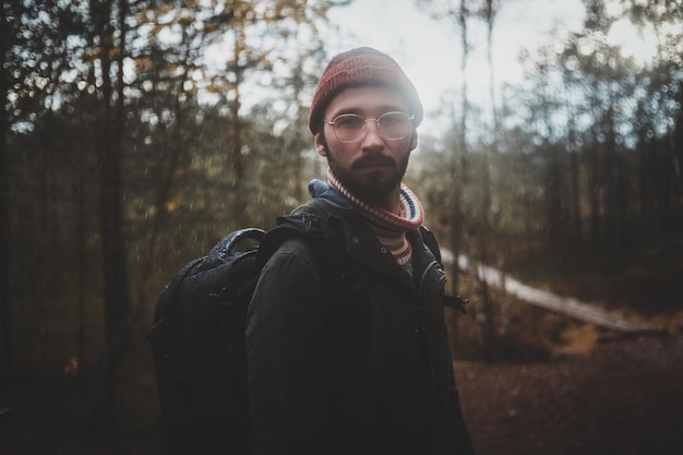 Retrato de jovem hipster barbudo com mochila na floresta de outono.