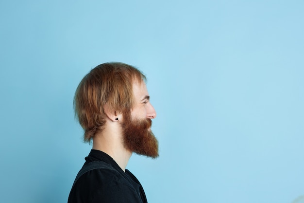 Retrato de jovem homem caucasiano parece sonhador, bonito e feliz. Olhando para cima e pensando no fundo azul do estúdio. Copyspace para sua publicidade. Conceito de futuro, alvo, sonhos, visualização.