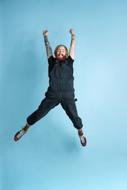 Foto grátis retrato de jovem homem caucasiano parece sonhador, bonito e feliz. pulando. rindo sobre fundo azul do estúdio. copyspace para sua publicidade. conceito de futuro, alvo, sonhos, visualização.