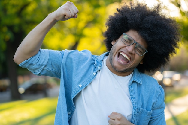 Foto grátis retrato de jovem latino comemorando a vitória ao ar livre. conceito urbano. conceito de sucesso.