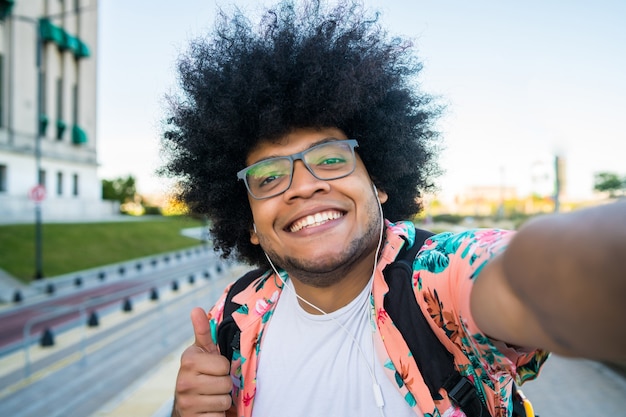 Retrato de jovem latino tirando uma selfie em pé ao ar livre na rua
