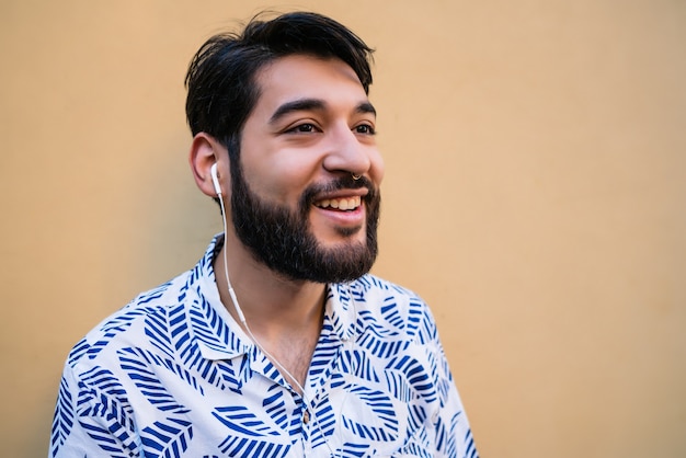 Foto grátis retrato de jovem latino vestindo roupas de verão e ouvindo música com fones de ouvido contra o espaço amarelo.