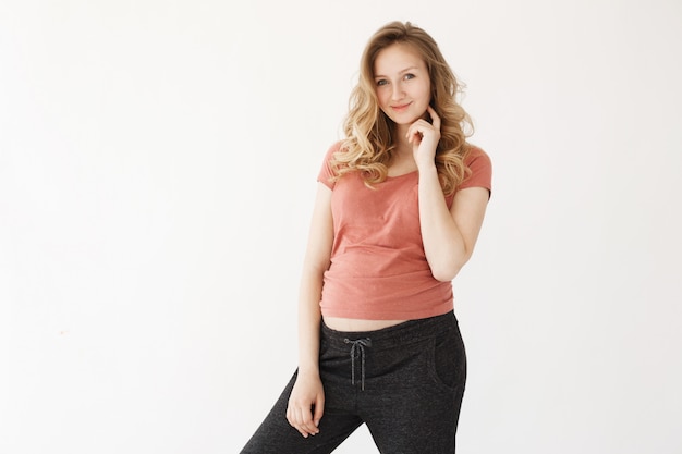 Retrato de jovem mãe feliz com cabelo loiro em casual camiseta vermelha e calça preta, segurando a mão perto do rosto