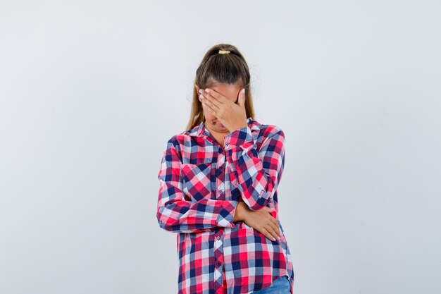 Retrato de jovem mantendo a mão no rosto em uma camisa casual e olhando para a frente com depressão