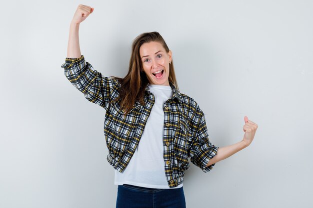 Retrato de jovem mostrando gesto de vencedor em camiseta, jaqueta, jeans e com sorte vista frontal