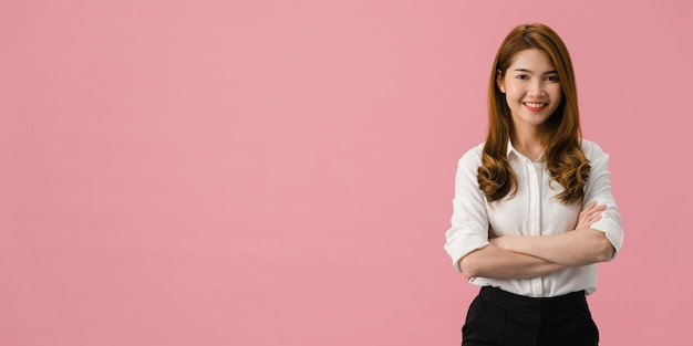 Retrato de jovem mulher asiática com expressão positiva, braços cruzados, sorriso largo, vestida com roupas casuais e olhando para a câmera sobre fundo rosa.