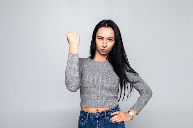 Retrato de jovem mulher morena dominante, mostrando o punho na parede cinza