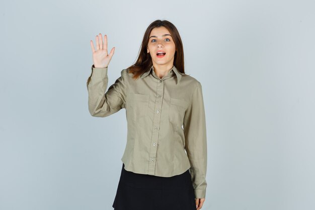 Retrato de jovem mulher mostrando a palma da mão na camisa, saia e olhando maravilhada vista frontal