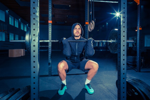 Retrato de jovem musculoso em forma super em forma, malhando na academia com barra