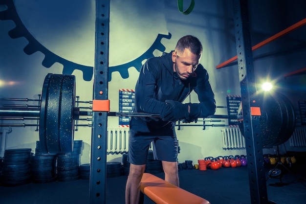 Retrato de jovem musculoso em forma super em forma, malhando na academia com uma barra no azul