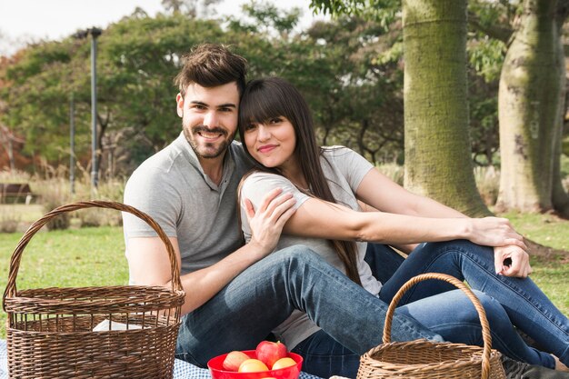 Retrato, de, jovem, par sorrindo, sentando, parque, com, frutas, e, cesta piquenique