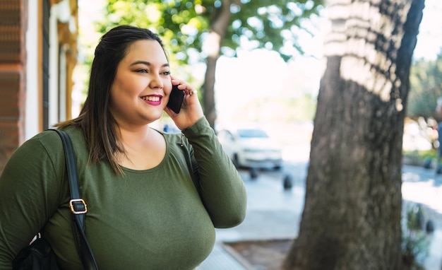 Retrato de jovem plus size mulher sorrindo enquanto fala ao telefone, ao ar livre na rua. conceito urbano.