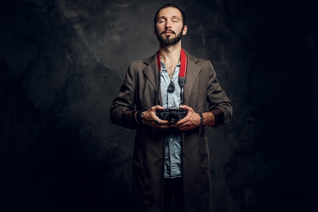 Retrato de jovem repórter barbudo com câmera fotográfica no estúdio fotográfico escuro.