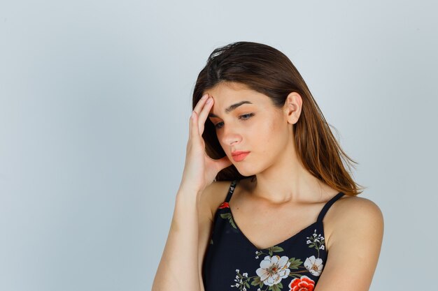 Retrato de jovem segurando a mão no rosto em um top floral e parecendo chateado