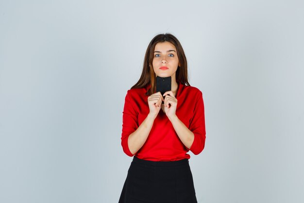 Foto grátis retrato de jovem segurando um telefone celular embaixo do queixo com uma blusa vermelha