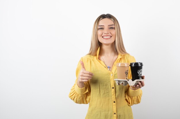 Retrato de jovem segurando xícaras de café e desistir de polegares.