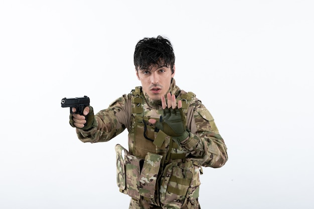 Retrato de jovem soldado camuflado com arma na parede branca