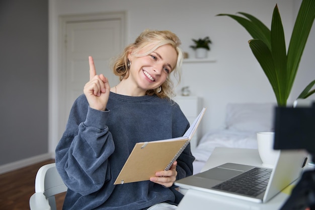 Foto grátis retrato de jovem sorridente mulher carismática levantando um dedo ensinando leitura on-line do caderno