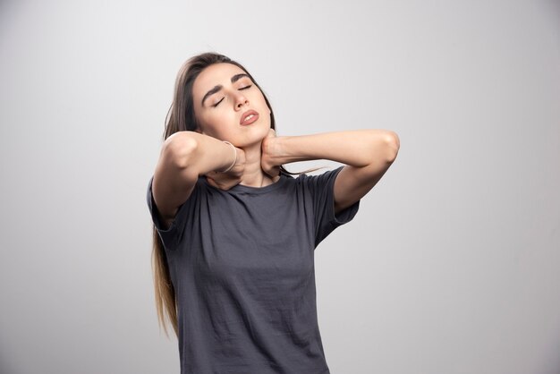 Retrato de jovem tocando seu pescoço posando sobre fundo cinza.