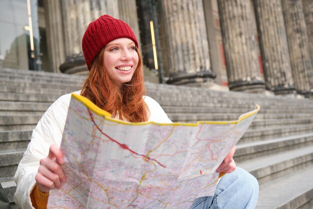 Retrato de jovem turista ruiva senta-se com mapa de papel e procura uma rota para atrair turismo