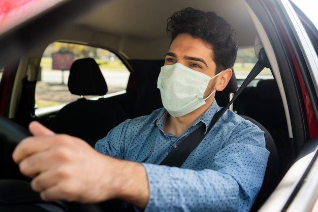 Foto grátis retrato de jovem usando máscara facial enquanto dirigia seu carro a caminho do trabalho. conceito de transporte. novo conceito de estilo de vida normal.