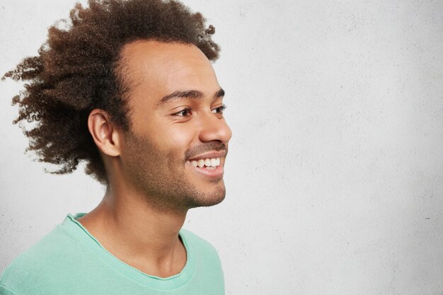 Retrato de lado de um homem afro-americano alegre com cabelo crespo, sorrindo gentilmente