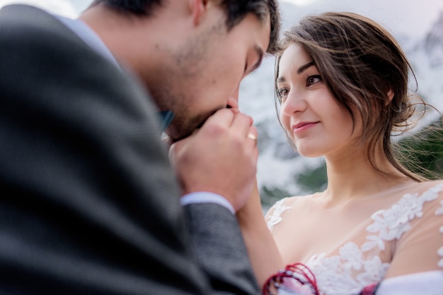 Retrato de loucamente apaixonado casal de noivos, noiva e noivo ao ar livre, homem está beijando as mãos da mulher