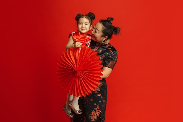 Retrato de mãe e filha asiático isolado em uma parede vermelha em roupas tradicionais