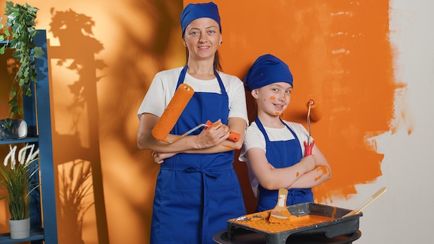 Foto grátis retrato de mãe e filho pintando paredes com tinta de cor laranja, usando equipamentos de renovação e ferramentas de escova de rolo para redecorar o interior do apartamento. trabalho doméstico de melhoria de decoração para casa.