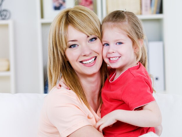 Retrato de mãe feliz e sorridente alegre com a filha em um abraço - dentro de casa