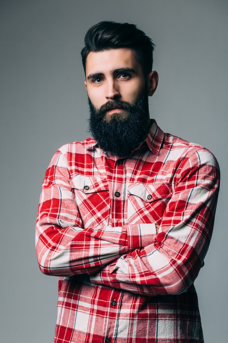 Foto grátis retrato de masculinidade. retrato de um jovem bonito barbudo em pé contra uma parede cinza