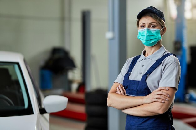 Retrato de mecânico de automóveis feminino em pé com os braços cruzados enquanto usava máscara facial protetora na oficina