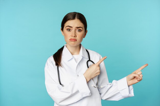 Retrato de médico decepcionado mulher trabalhadora médica apontando os dedos para a direita e parecendo triste pesar...