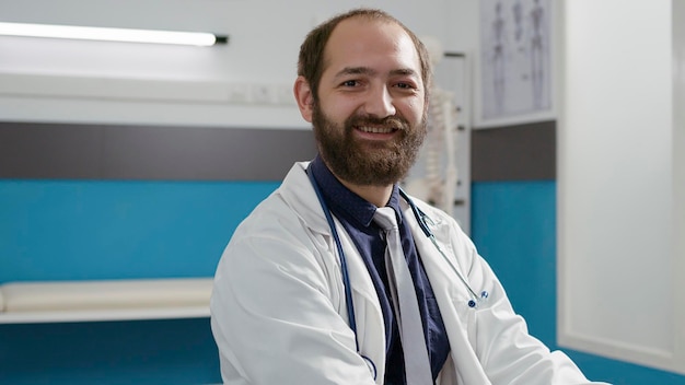 Foto grátis retrato de médico masculino com uniforme usando laptop no armário, trabalhando em consultas de check-up na mesa. especialista em saúde com estetoscópio, ajudando com medicamentos prescritos e tratamento.