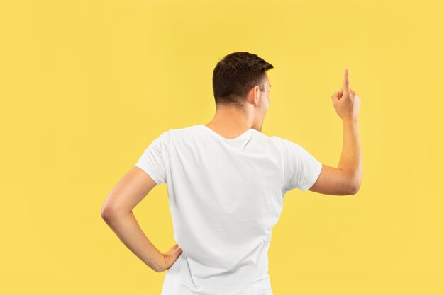 Retrato de meio comprimento de jovem caucasiano sobre fundo amarelo do estúdio. Lindo modelo masculino na camisa. Conceito de emoções humanas, expressão facial, vendas, anúncio. Mostrando e apontando algo.